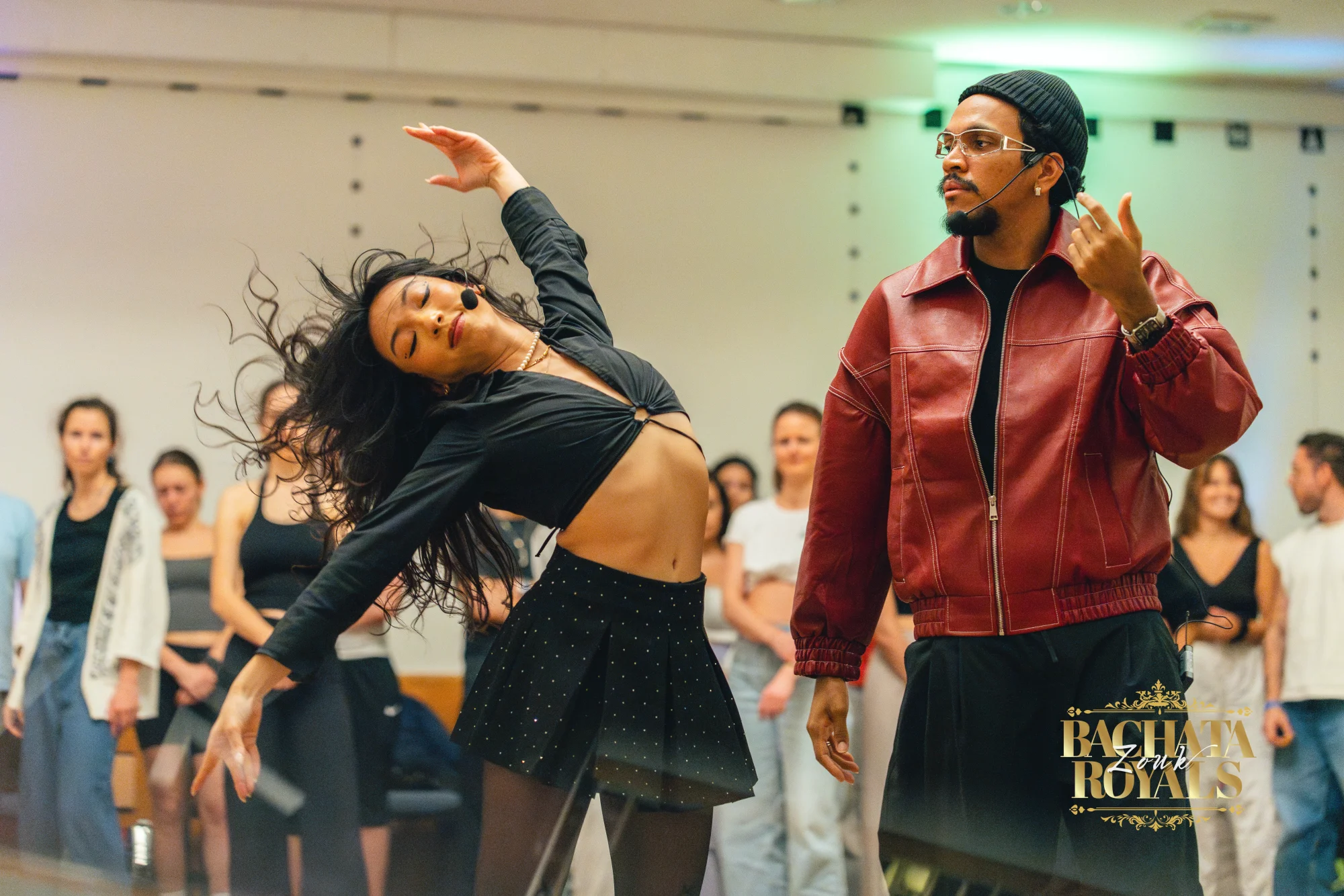 Artists mit Ansteckmikrofon zeigen im Workshop eine Zouk-Bewegung, Teilnehmende sehen zu