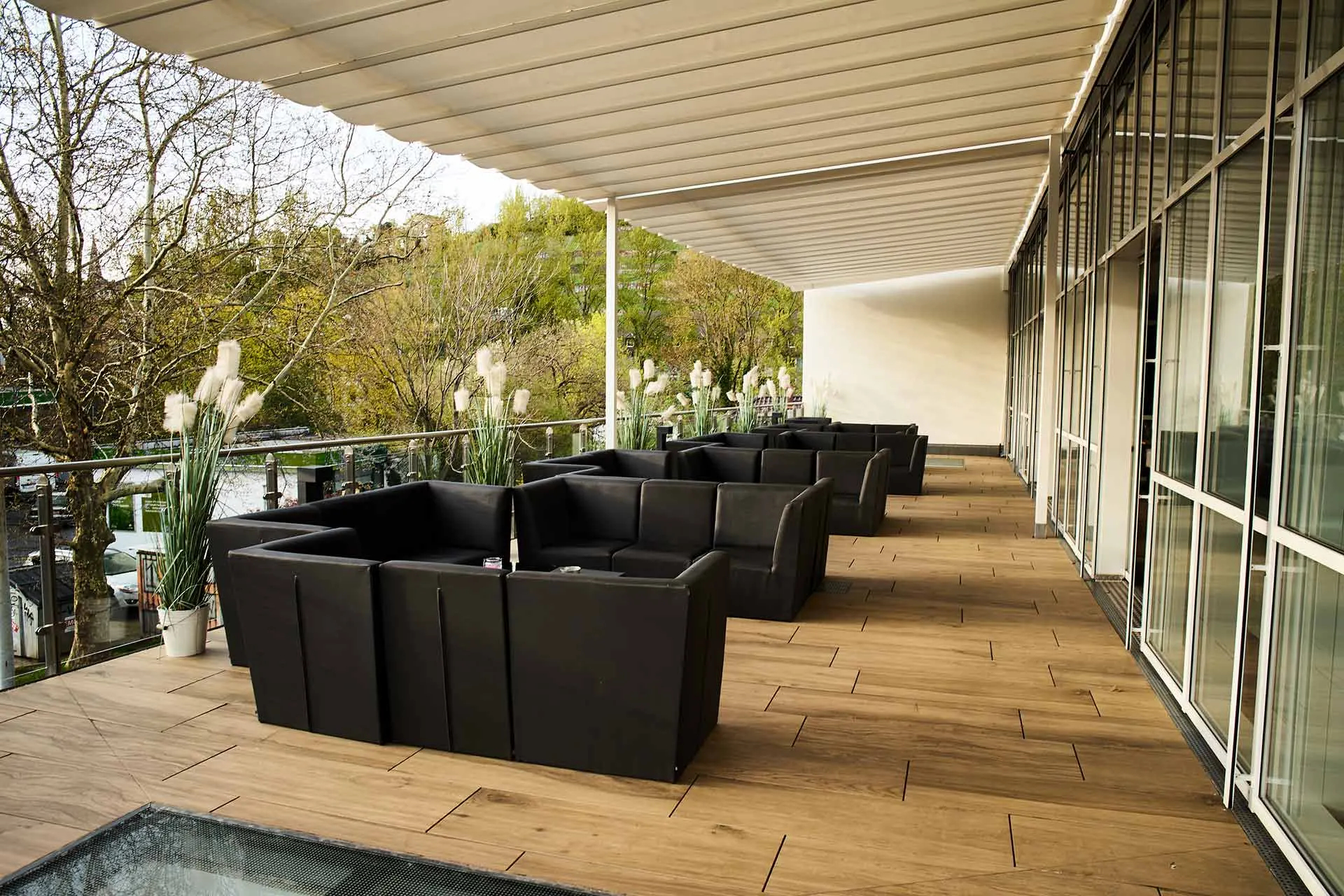 Überdachte Terrasse des Ballhaus Freiburg mit dunklen Loungemöbeln und Blick ins Grüne