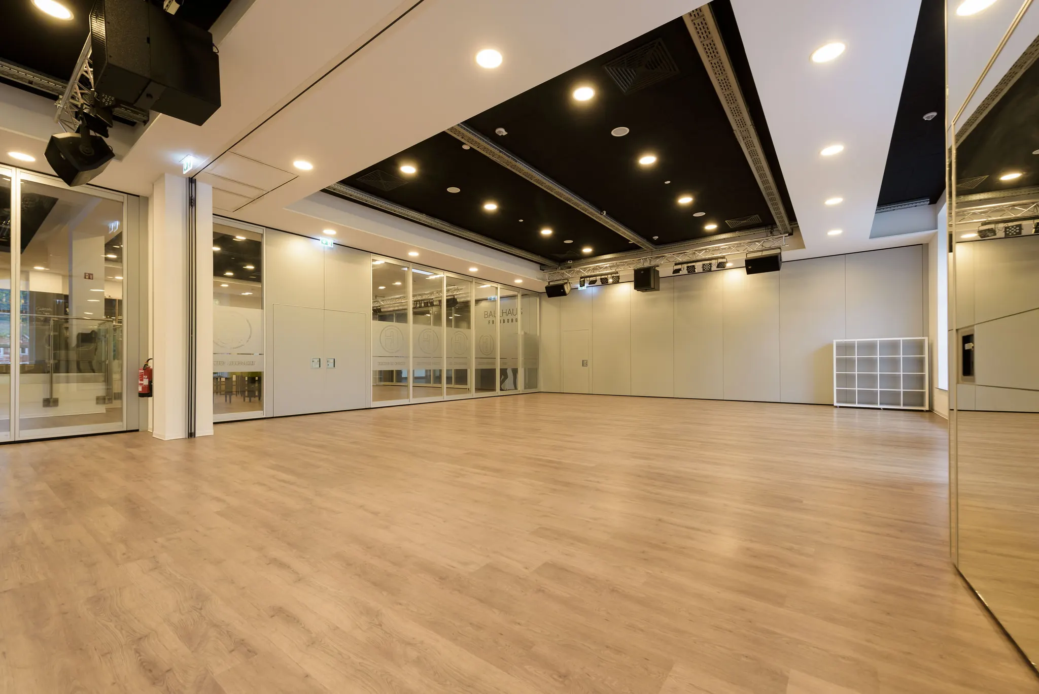 Leerer Tanzsaal des Ballhaus Freiburg mit hellem Holzboden, Spiegelwand und Traversen mit Scheinwerfern unter der Decke